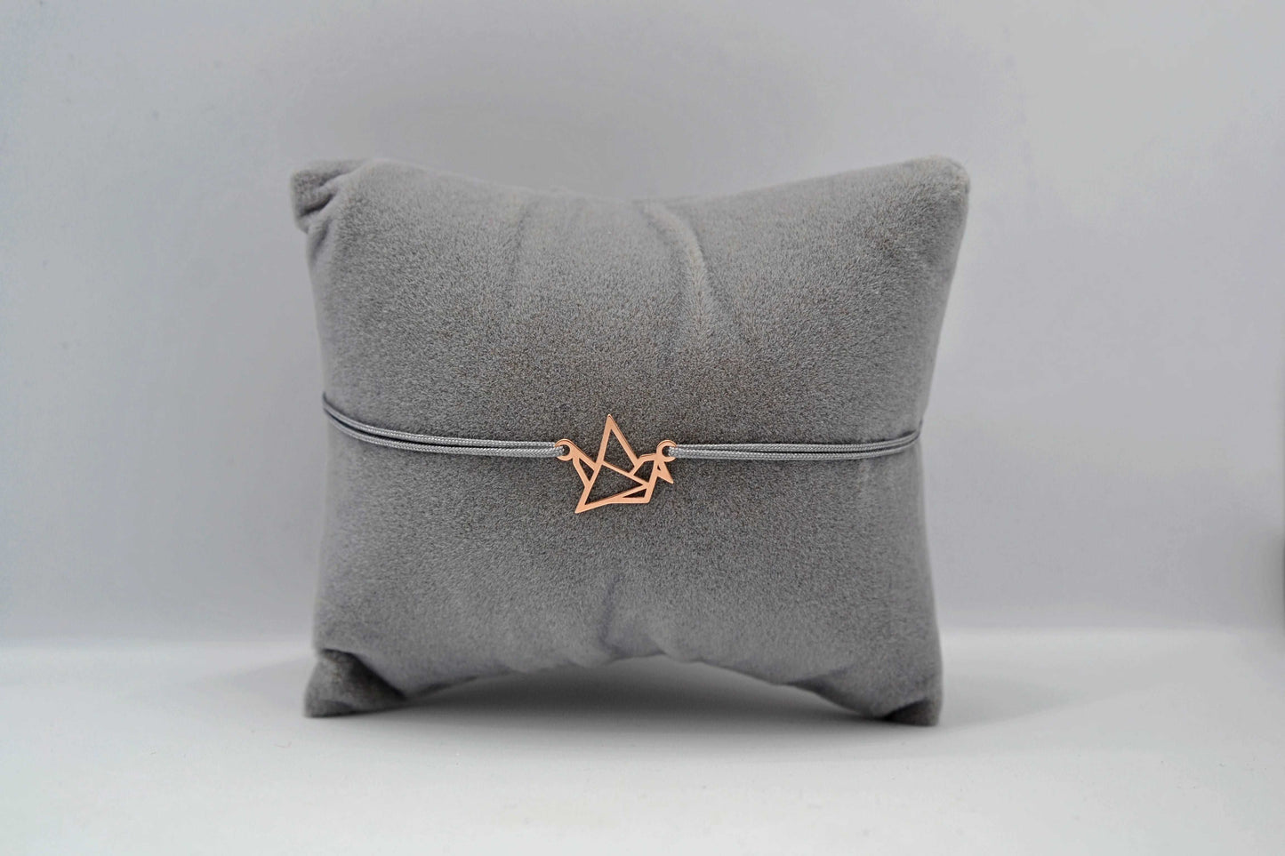 Kranich Armband roségold mit grauem Band auf einem grauen Schmuckkissen