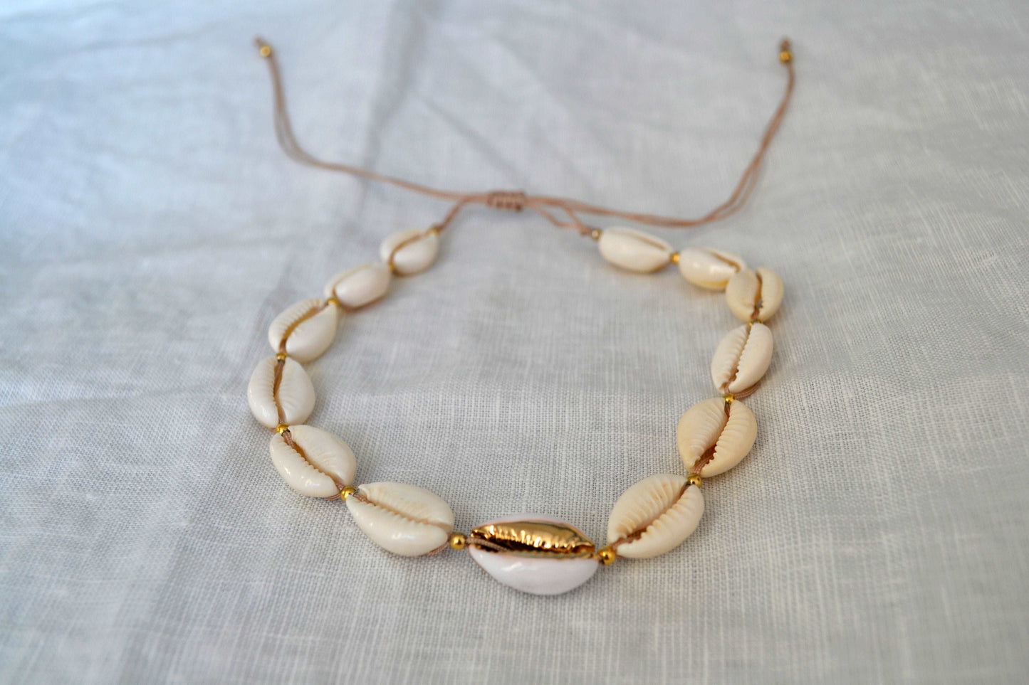 Muschel Choker mit goldenen Perlen zwischen den Muscheln und beigem Band auf einer weißen Tischdecke