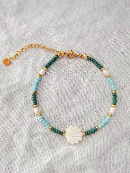 Muschel Fußkettchen mit einer weißen Jakobsmuschel, kleinen Glasperlen in grün, hellblau und gold und weißen Süßwasserperlen. Fußkette auf einem weißen Leinentuch