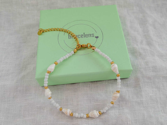 Eine Muschel Fußkette in gold und weiß liegt auf einer mintgrünen Schmuckschachtel mit bracelens Logodruck
