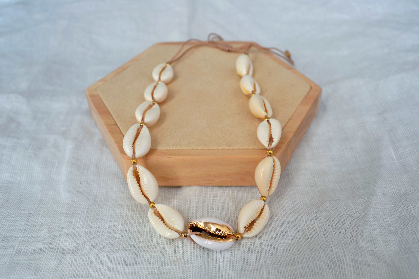 Präsentationsfoto Muschelkette mit goldenen Akzenten auf einem Holz Sechseck