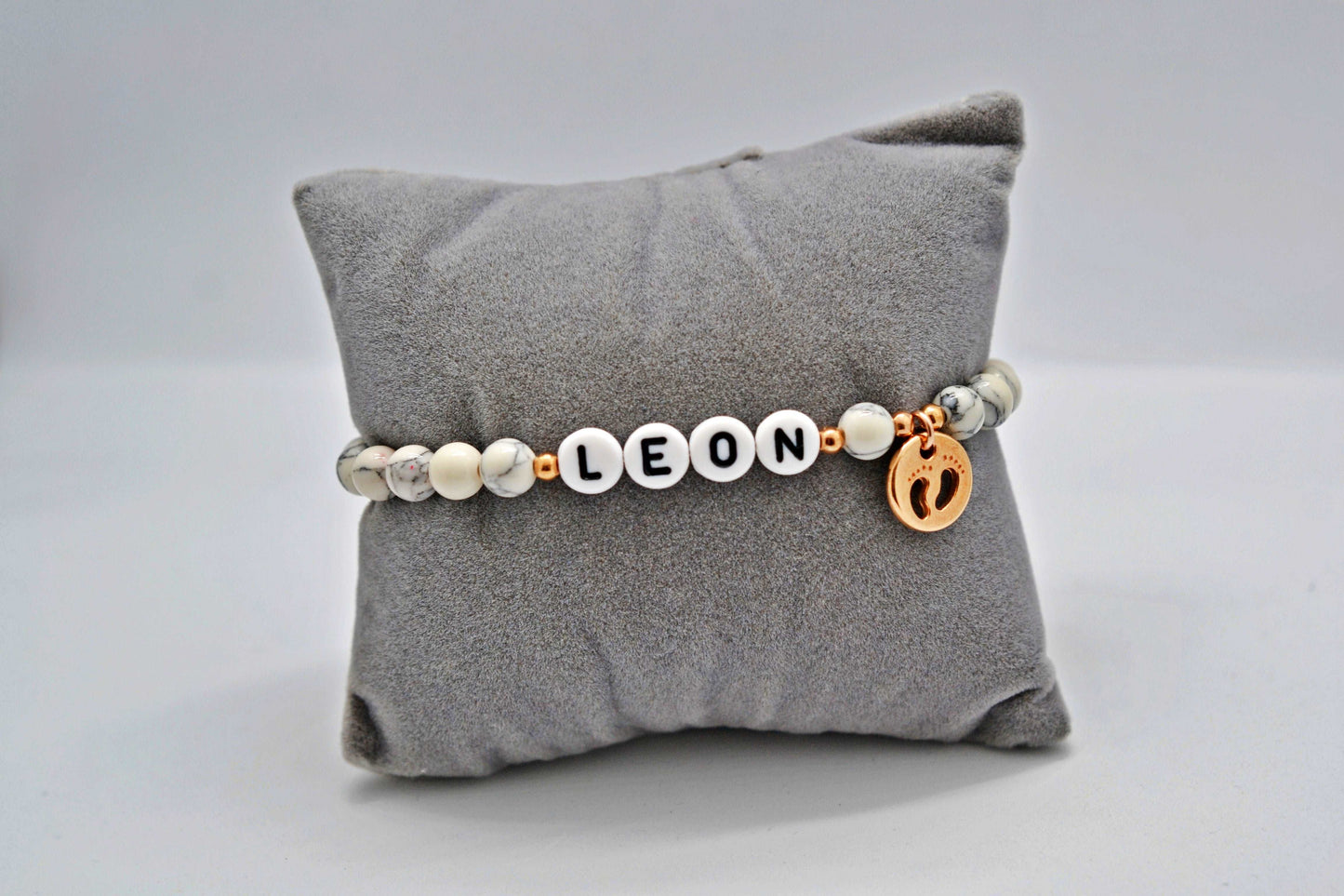 Armband für Mamas mit Wunschnamen und Babyfüßchen Anhänger auf einem grauen Schmuckkissen