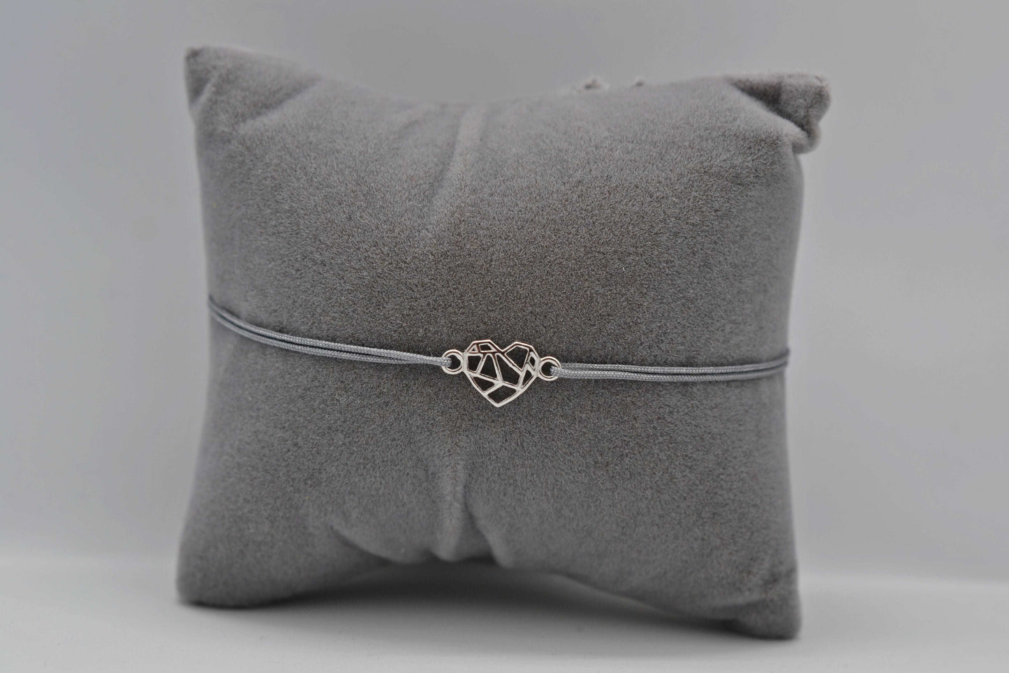 Silbernes Origami Herz Armband mit grauem Band auf einem grauen Schmuckkissen