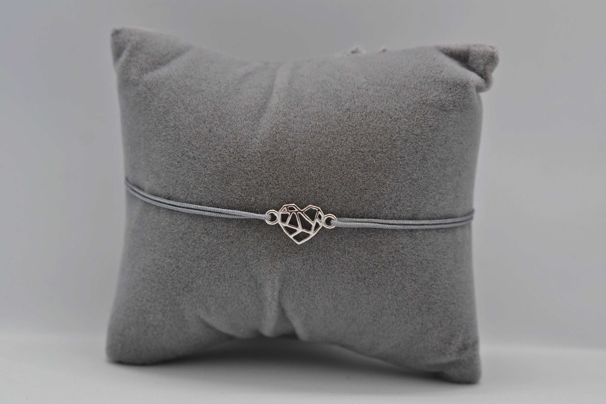 Silbernes Origami Herz Armband mit grauem Band auf einem grauen Schmuckkissen