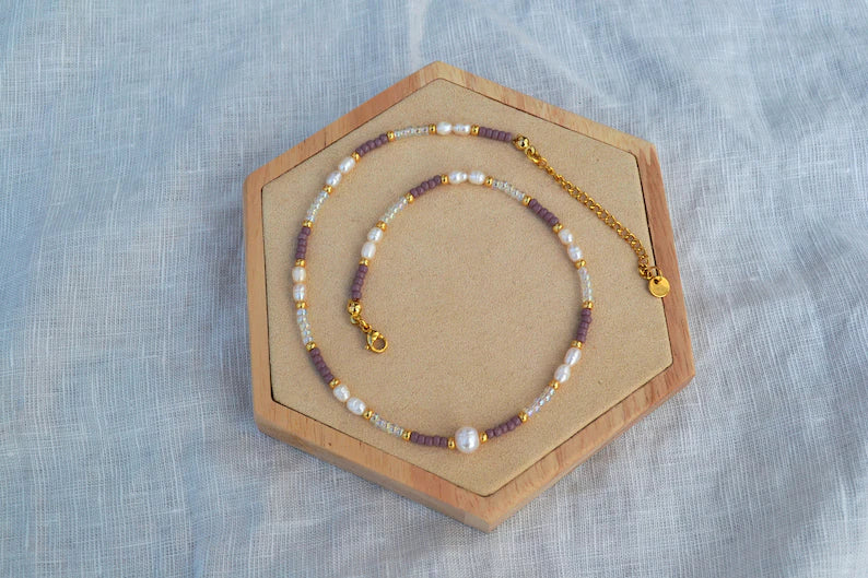 Bunter Perlen Choker aus Glasperlen in lila, gold und durchsichtig, Süßwasserperlen und Edelstahlelementen. Von oben fotografiert auf einem Holz Sechseck