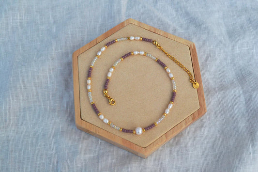 Bunter Perlen Choker aus Glasperlen in lila, gold und durchsichtig, Süßwasserperlen und Edelstahlelementen. Von oben fotografiert auf einem Holz Sechseck