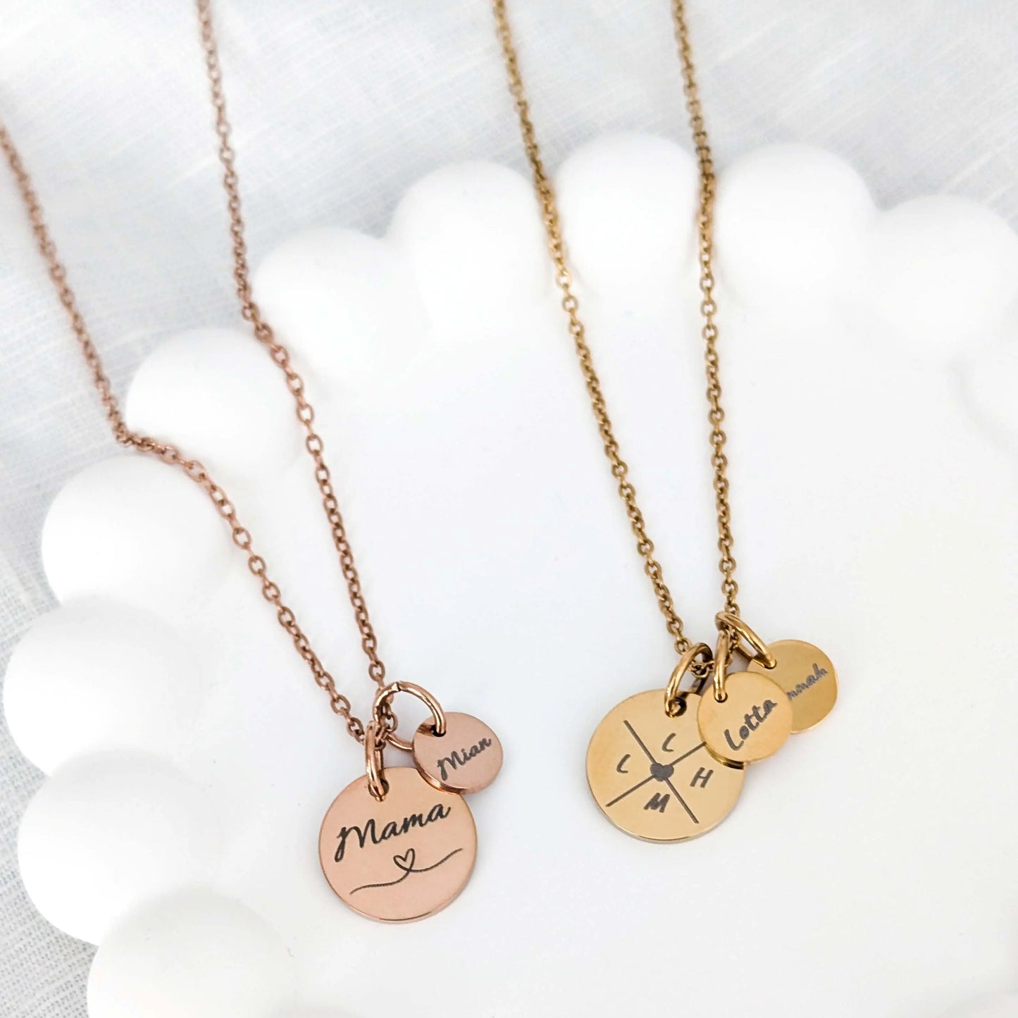Zwei personalisierte Gravurketten in roségold und gold liegen nebeneinander auf einem weißen Untersetzer