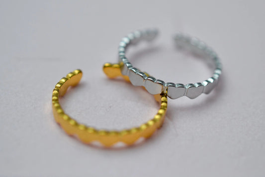 Zwei Edelstahl Ringe aus kleinen Herzen in Nahaufnahme. Ein Ring in gold und daran gelehnt ein Ring in Silber.