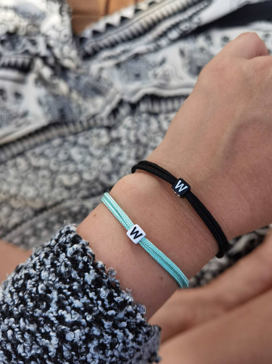 Tragefoto zwei Surfer Armbänder personalisiert am Arm einer Frau. Ein mintgrünes Armband mit weißer Buchstabenperle "W" und ein schwarzes Armband mit schwarzer Buchstabenerle "W"