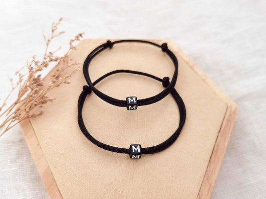 Zwei schwarze personalisierte Partnerarmbänder aus Segeltau beide mit Buchstaben "M" auf einem Holz Sechseck