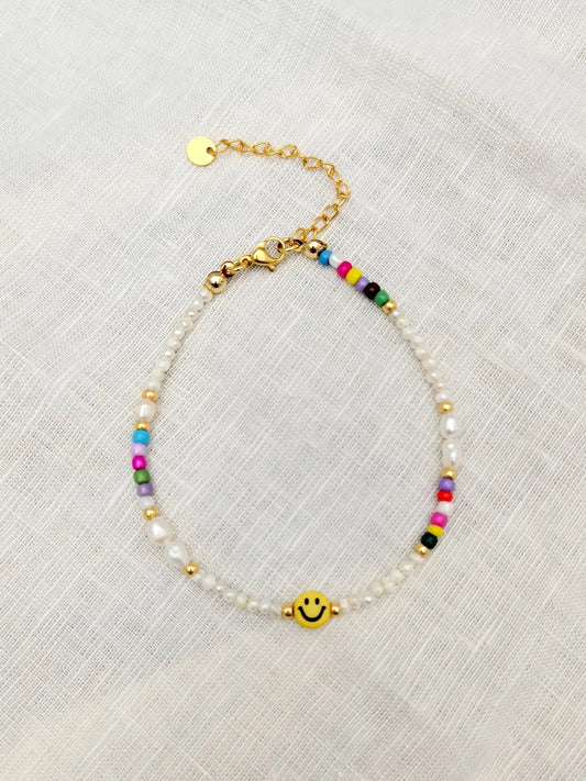 Fußkette mit gelbem Smiley, kleinen Süßwasserperlen und kleinen bunten Perlen fotografiert auf einem weißen Tuch