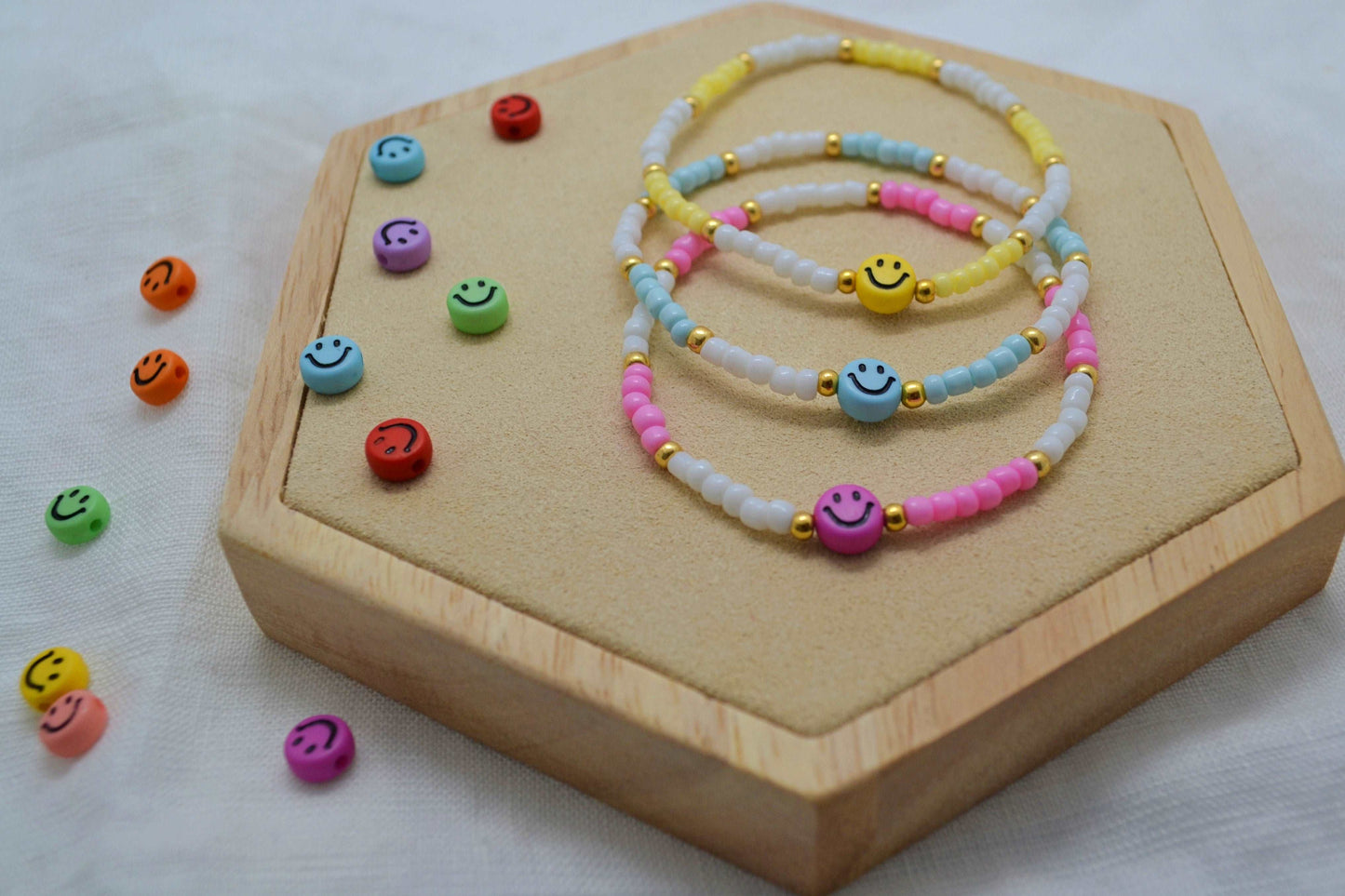 buntes Smiley Armband in rosa, blau und gelb übereinander gelegt auf einem Holz Sechseck. Daneben weitere bunte Smiley Perlen