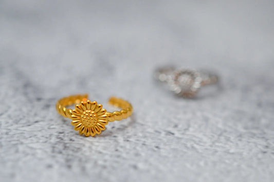 Nahaufnahme eines goldenen Sonnenblumen Rings. Im Hintergrund unscharf derselbe Ring in silber dargestellt