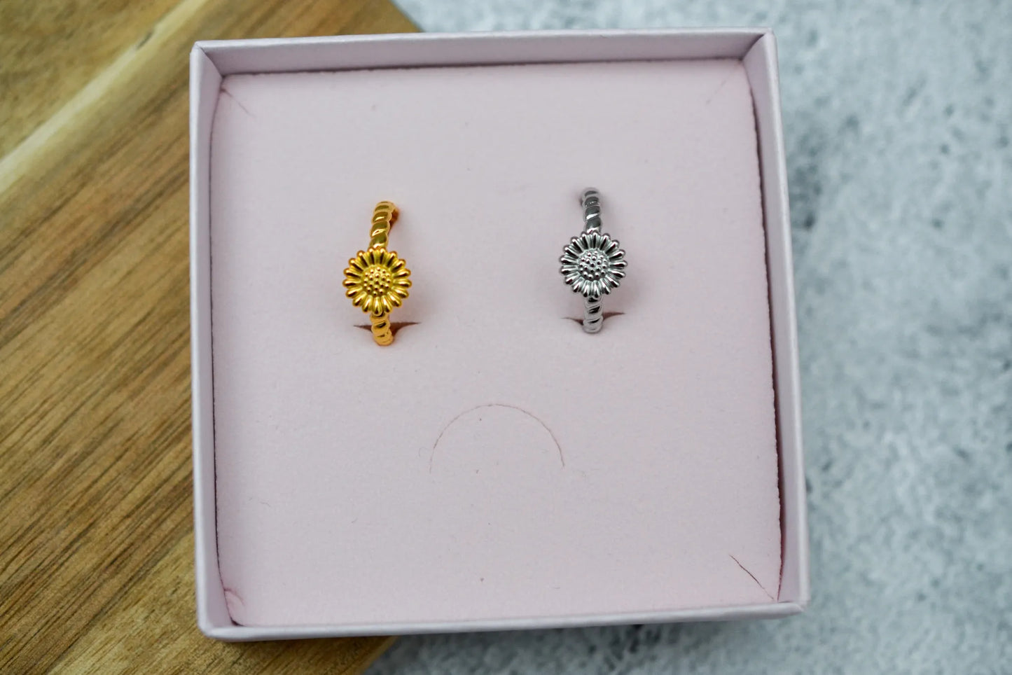Ein goldener und ein silberner Sonnenblume Ring nebeneinander in einer rosa Schmuckschachtel