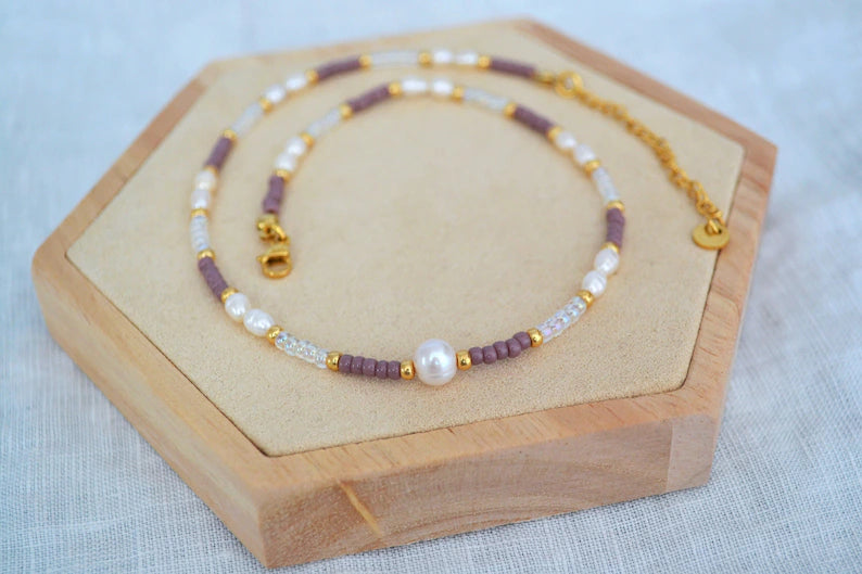 Bunter Perlen Choker aus Glasperlen in lila, gold und durchsichtig, Süßwasserperlen und Edelstahlelementen. Fotografiert auf einem Holz Sechseck