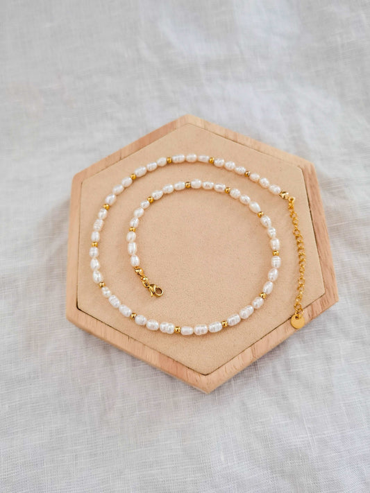 Eine Süßwasserperlenkette mit goldenen Akzenten liegt auf einem Holz Sechseck