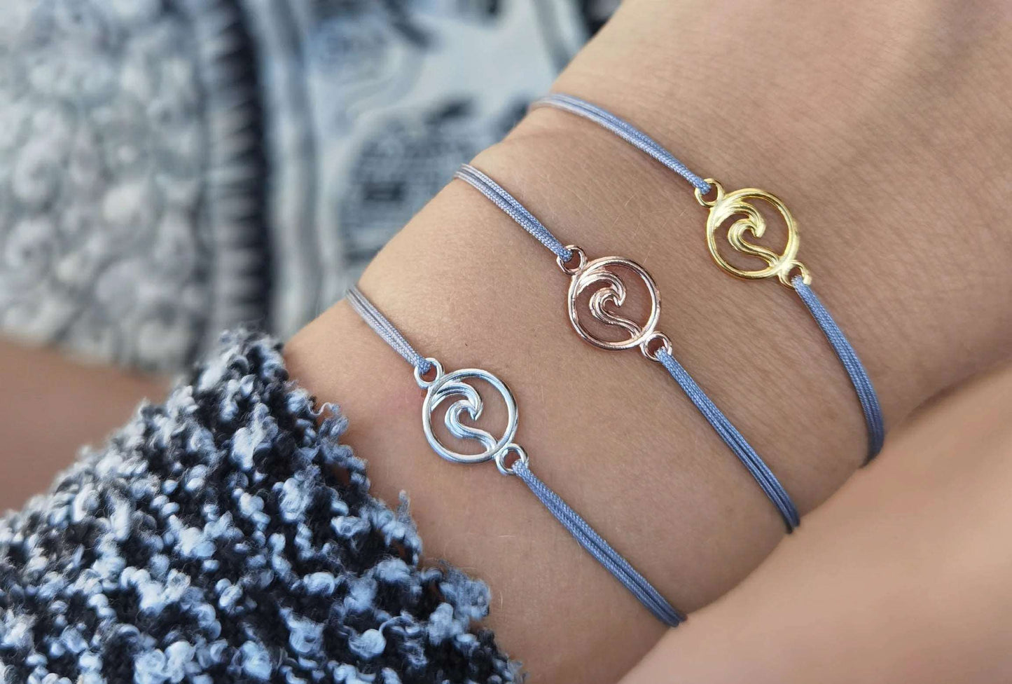 Tragefoto drei Armbänder mit einer Welle in silber, roségold und gold jeweils mit grauem Band am Handgelenk einer jungen Frau