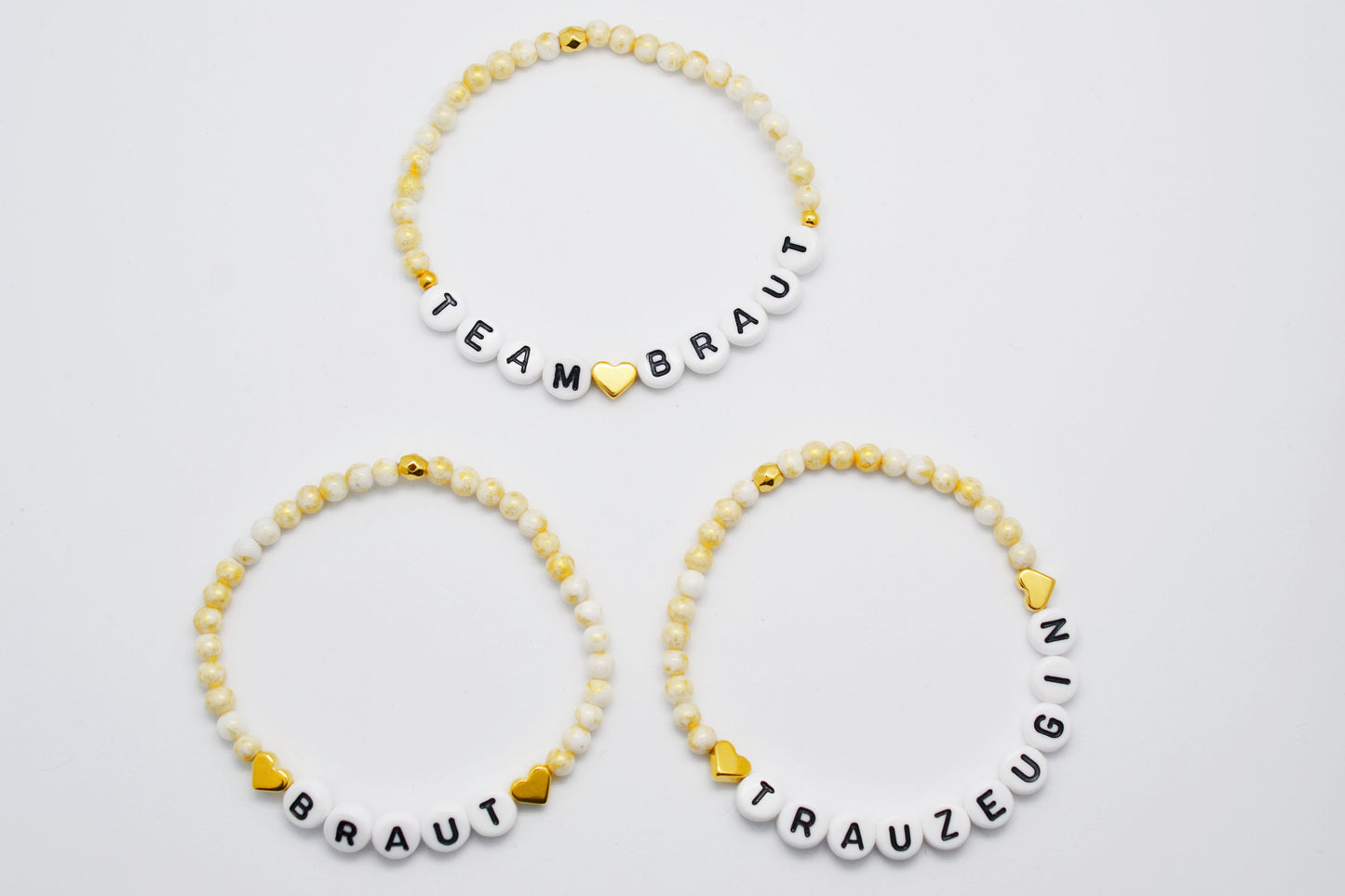 Drei personalisierbare JGA Perlenarmbänder mit goldenen Herzen und gold weiß Jadeperlen vor weißem Hintergrund