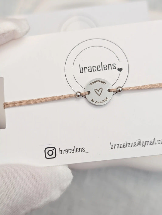 Personalisiertes Trauzeugin Armband mit runder Edelstahl-Gravur auf Schmuckkarte von bracelens, graviert mit Herz, Schriftzug „Trauzeugin“ und Datum, filigranes Armband auf beigem Band