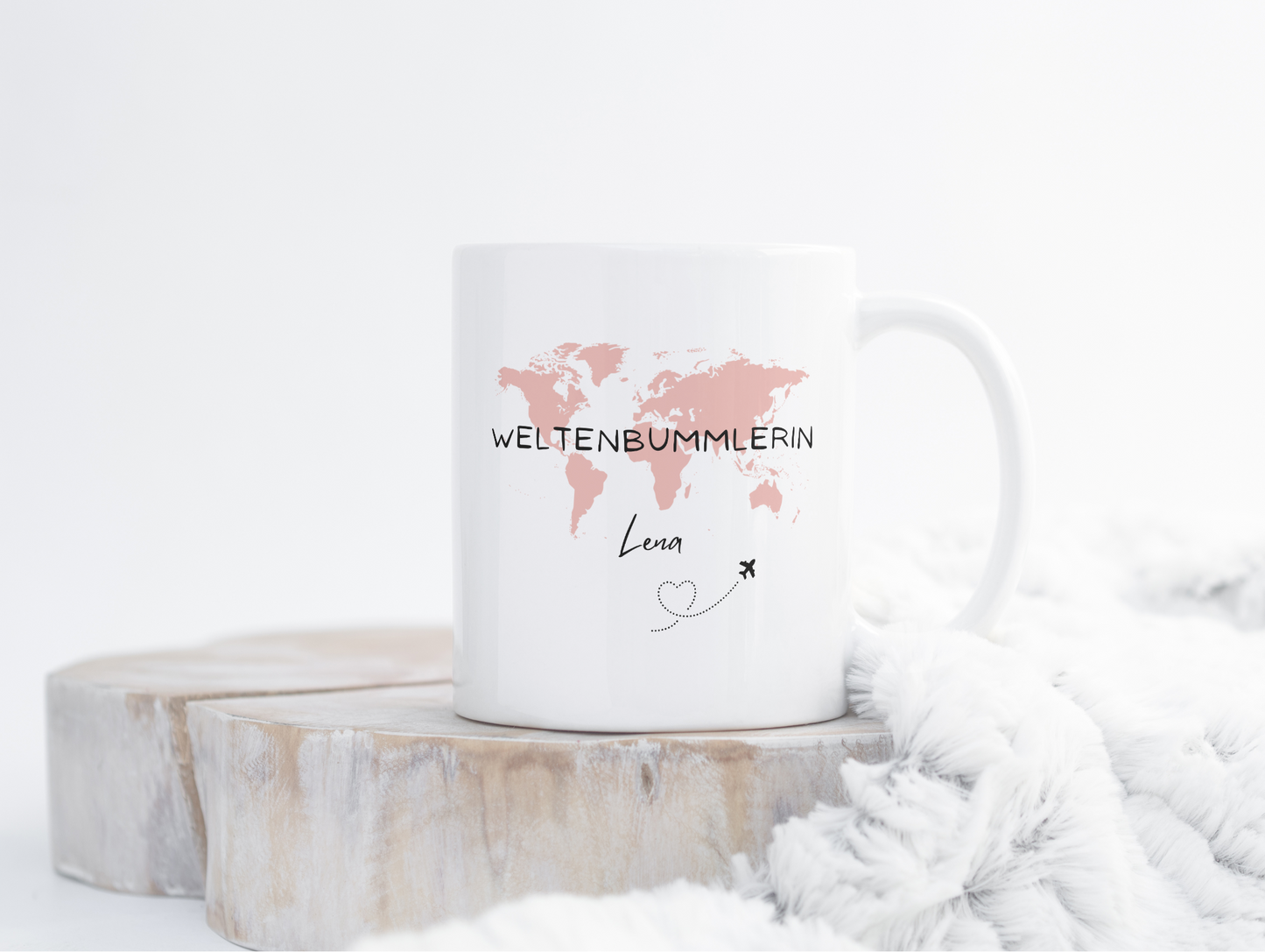 Weiße Tasse mit rosa Weltkarte und der Aufschrift "Weltenbummlerin Lena" auf einer Holzscheibe