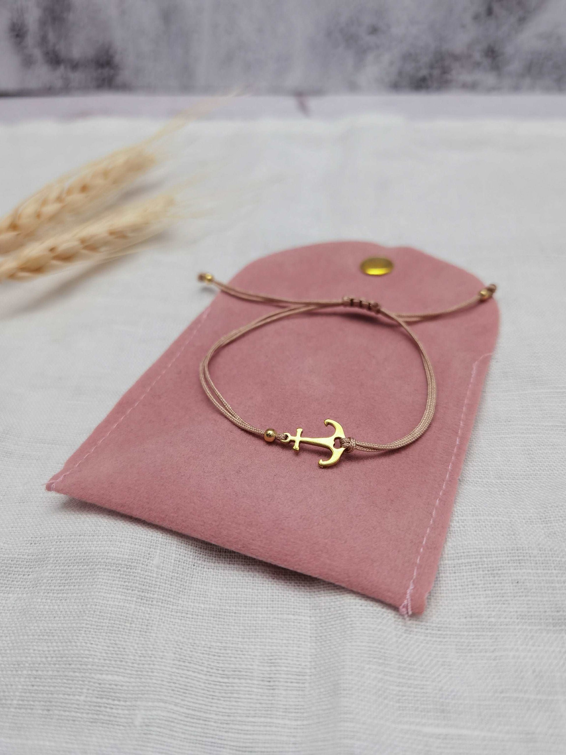 Anker Armband mit goldenem Edelstahl Anker und beigem Band auf einem rosa Schmucksäckchen
