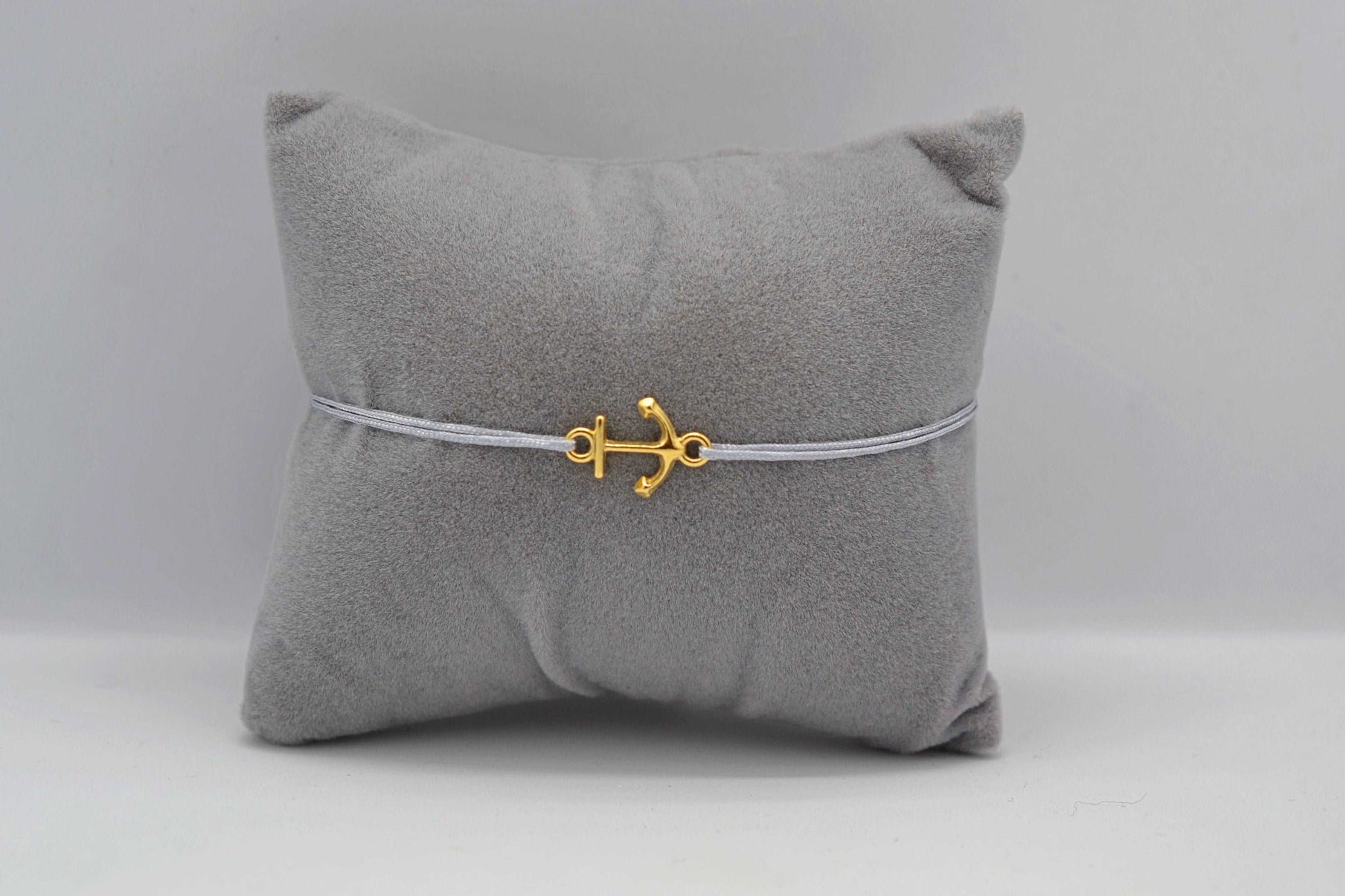Goldenes Anker Armband mit grauem Bank auf einem grauen Schmuckkissen