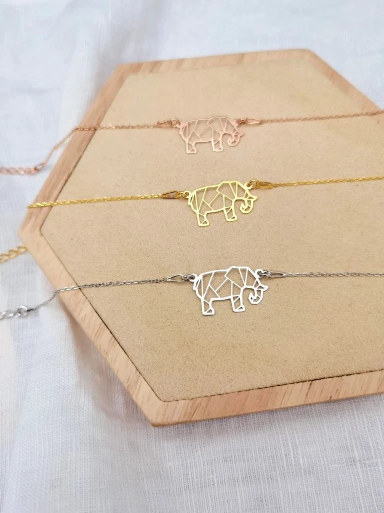 Drei Elefanten Armbänder in silber, gold und roségold liegen auf einem Holz Sechseck