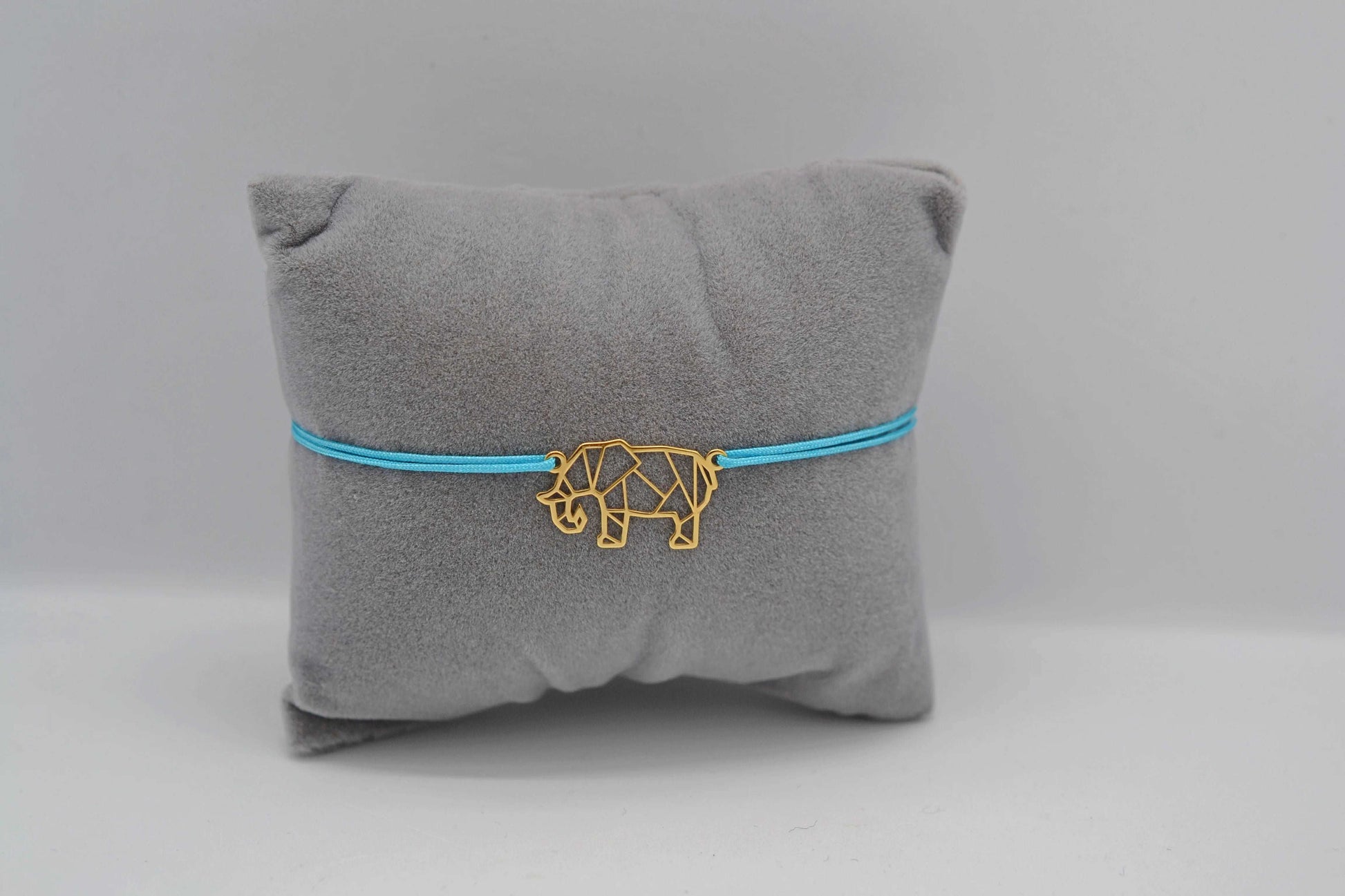 Armband Elefant gold mit türkisem Band auf grauem Schmuckkissen