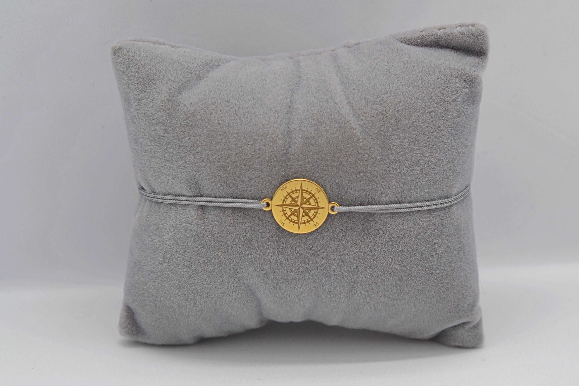 Goldenes Kompass Armband mit grauem Band auf einem grauen Schmuckkissen