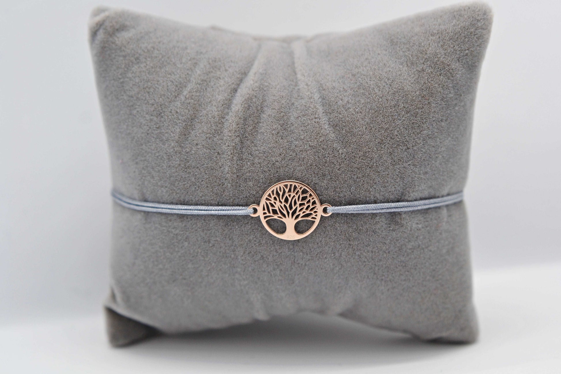 Lebensbaum Armband roségold mit grauem Band auf einem grauen Schmuckkissen