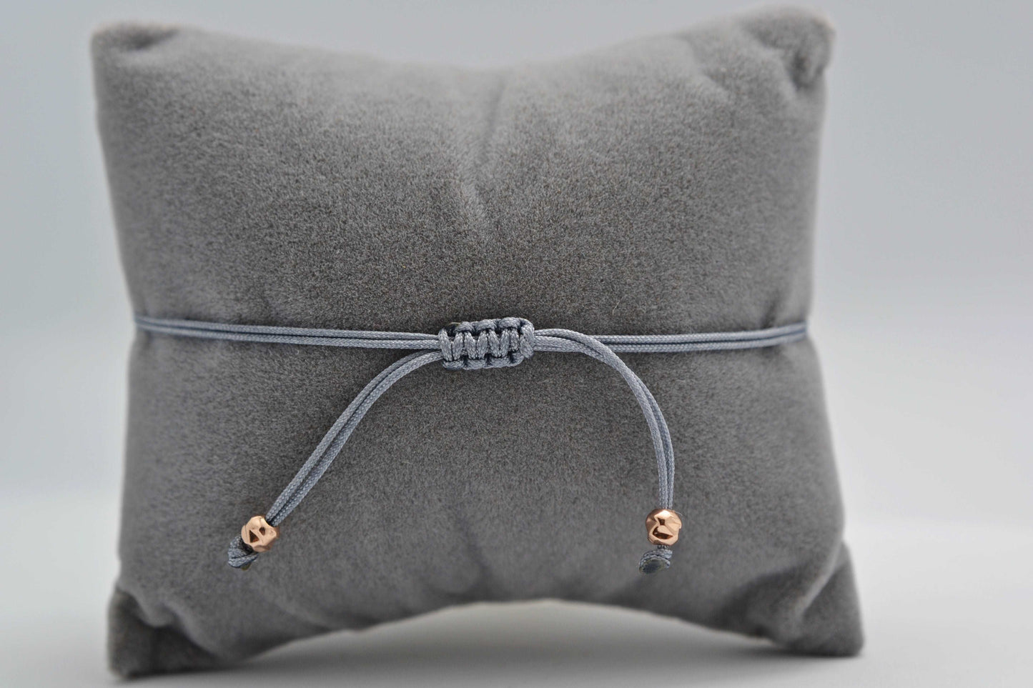 Makramee Verschluss graues Armband mit roségoldenen Perlen auf einem grauen Schmuckkissen