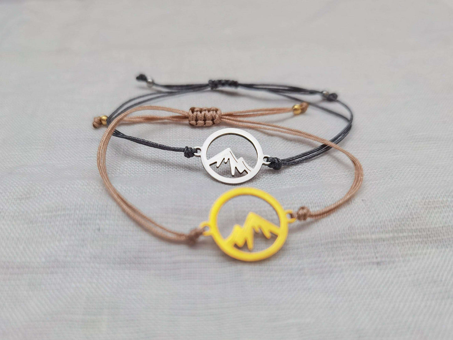 Nahaufnahme Berg Armband gold mit beigem Band und silber mit grauem Band vor weißem Hintergrund