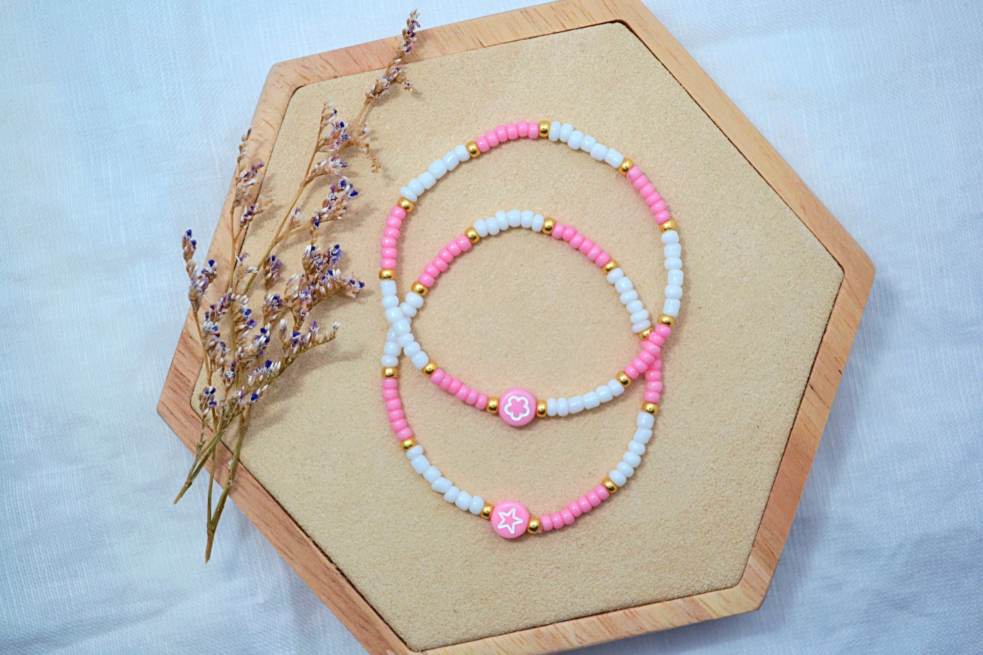 zwei Perlenarmbänder in rosa, weiß und gold mit einer Motivperle (1x Blume, 1x Stern)