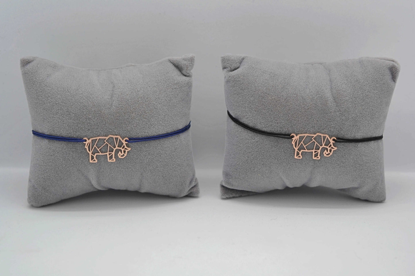 Armband Elefant roségold 1x mit blauem und 1x mit schwarzen Band jeweils auf einem grauen Schmuckkissen