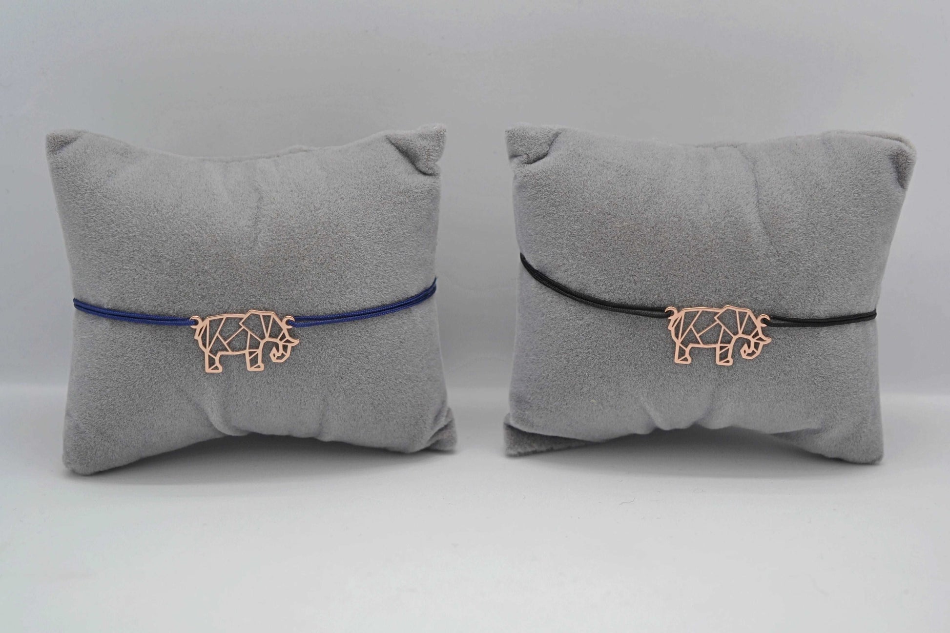 Armband Elefant roségold 1x mit blauem und 1x mit schwarzen Band jeweils auf einem grauen Schmuckkissen