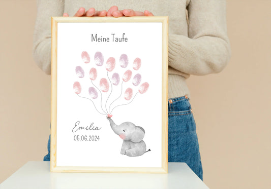 Personalisierbares Fingerabdruck Poster zur Taufe mit einem Elefanten der Ballons aus den Fingerabdrücken der Gäste hält. Personalisiert mit Namen und Datum. Bild in einem Holzrahmen wird von einer Frau gehalten