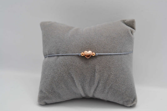 Herz Armband roségold mit grauem Band fotografiert auf einem grauen Schmuckkissen