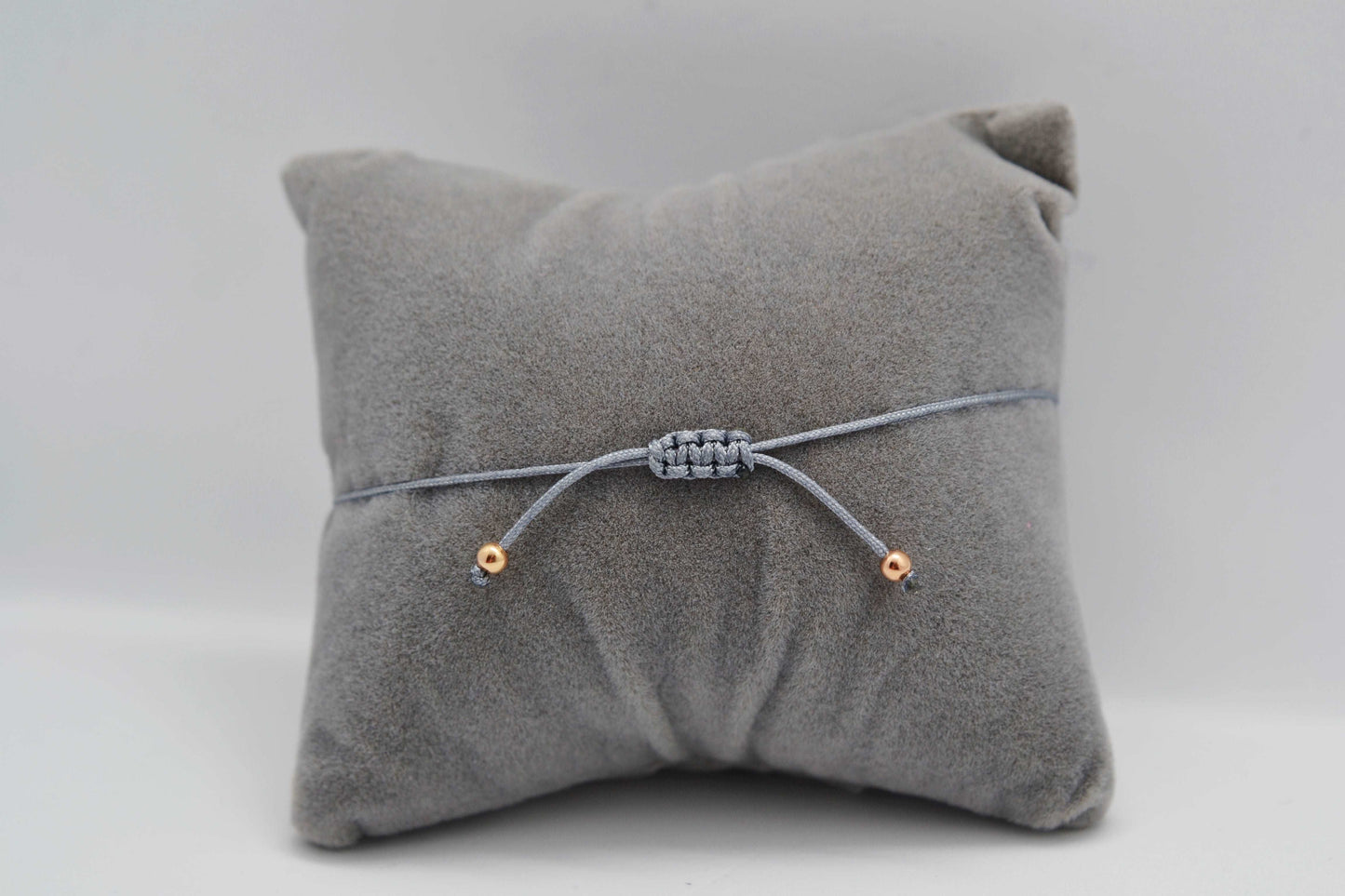 Makramee Verschluss Armband graues Band mit roségoldenen Perlen auf grauem Schmuckkissen