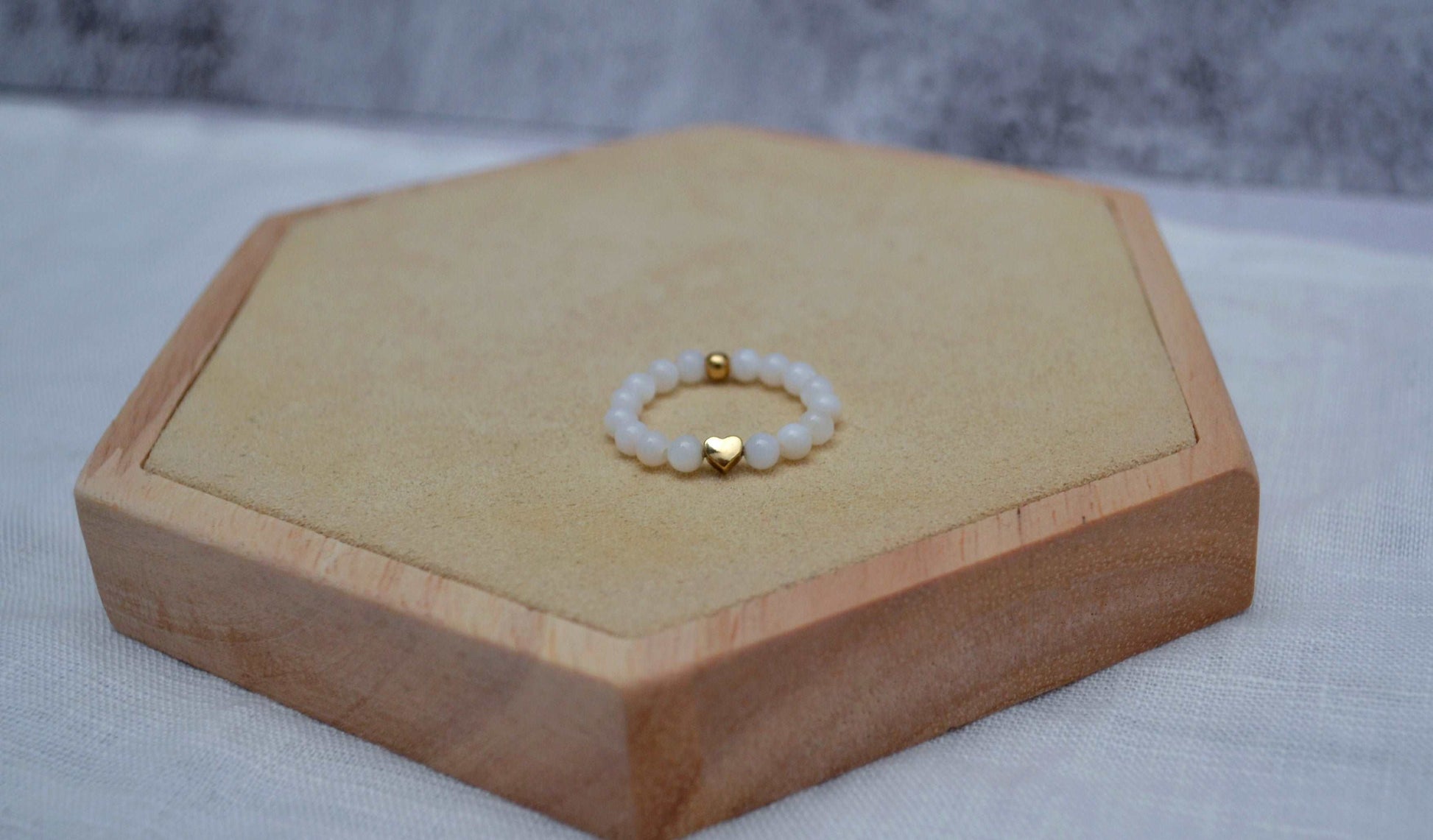 weißer Perlenring mit roségoldenem Herz auf einem Holz Sechseck