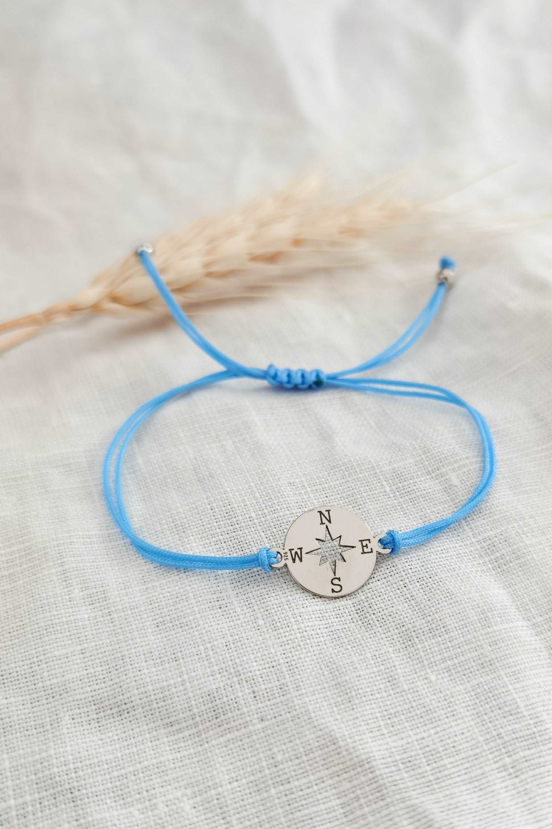 Silbernes Kompass Armband mit hellblauem Band vor weißem Hintergrund