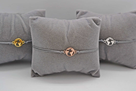 drei Armbänder mini Weltkarte in roségold, gold und silber mit grauem Band auf grauen Schmuckkissen