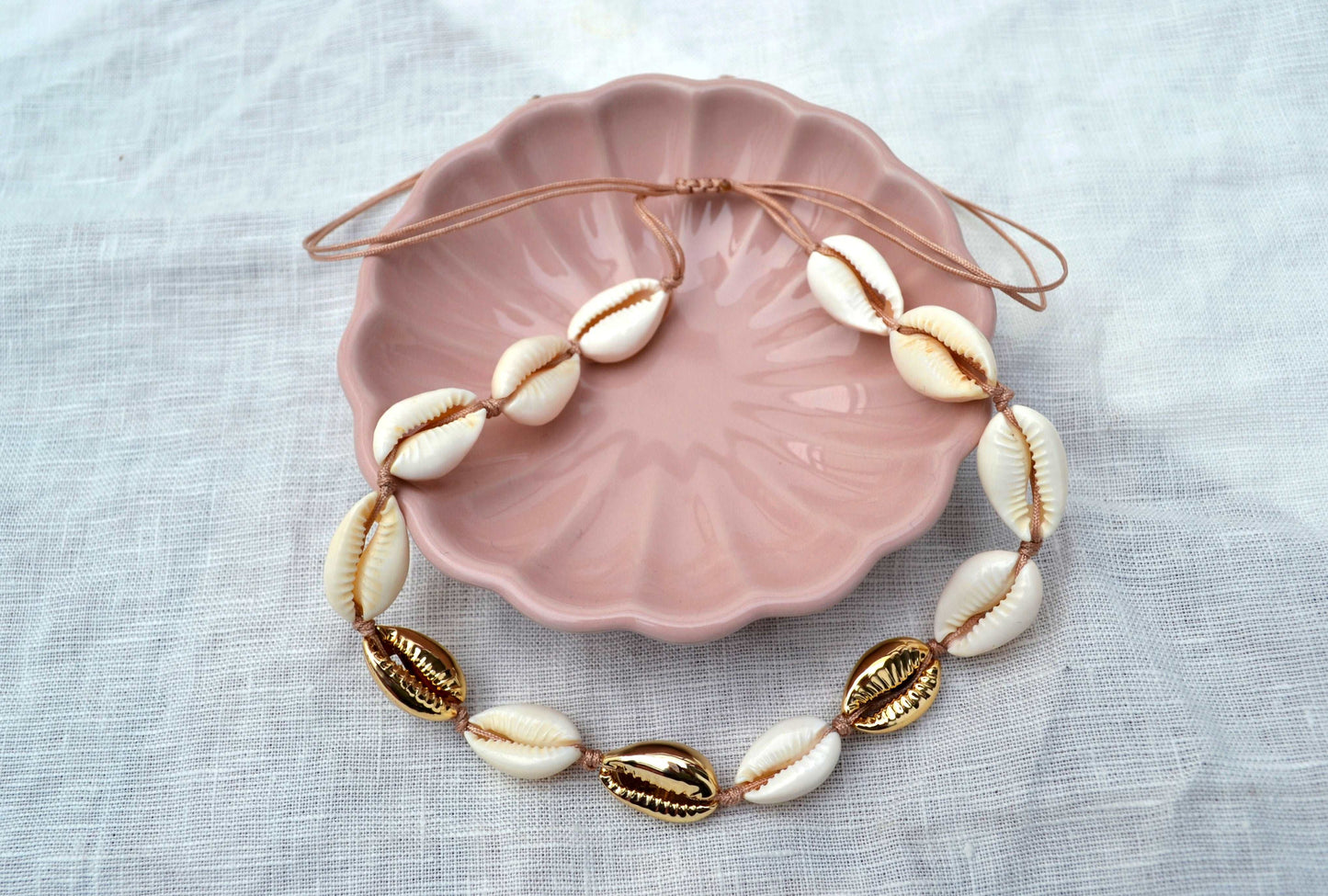 Kauri Muschel Kette mit goldenen und weißen Muscheln in einer rosa Schale