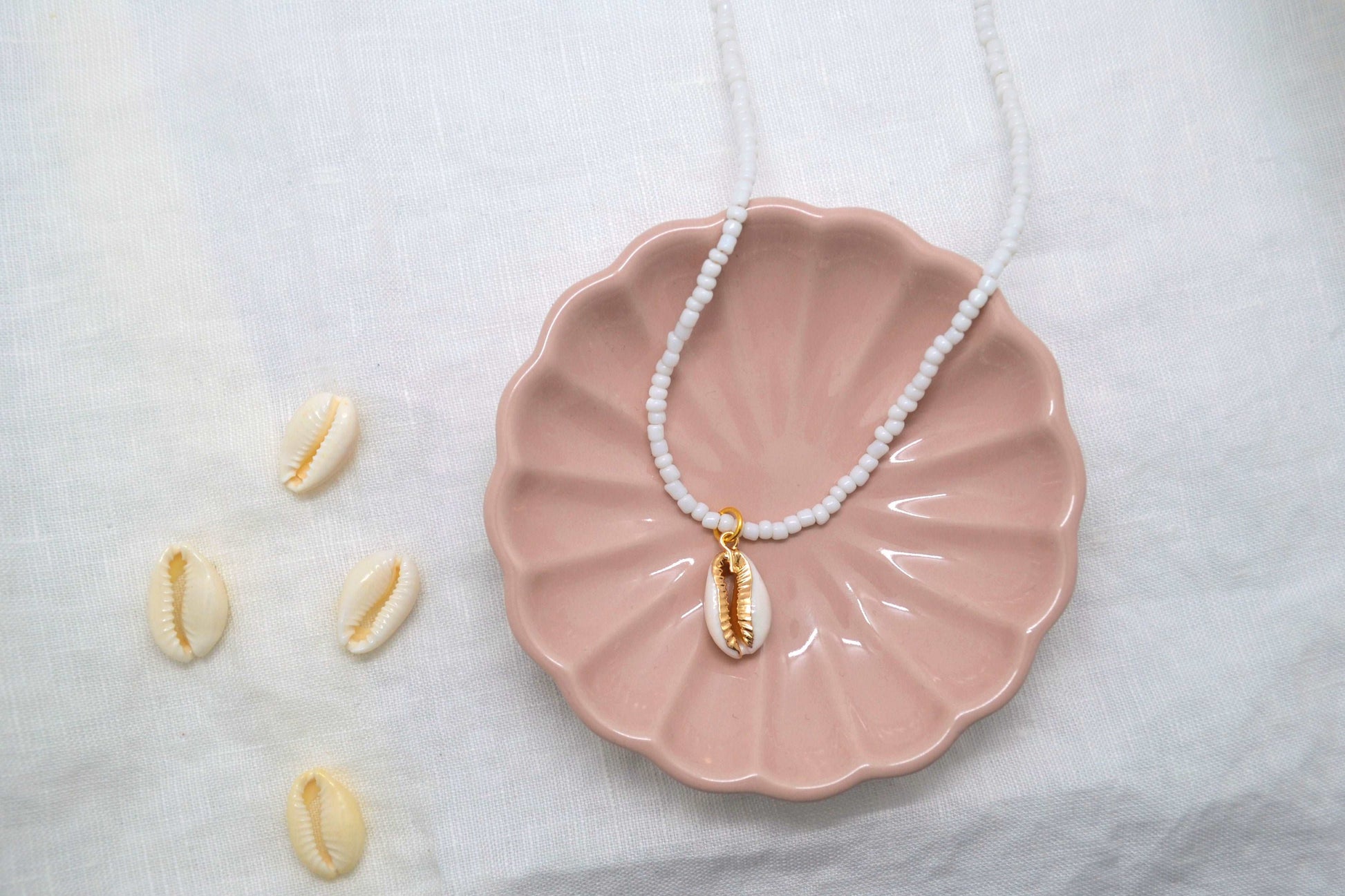 Muschelkette mit weißen Perlen und gold / weißem Muschelanhänger in einer rosa Schmuckschale