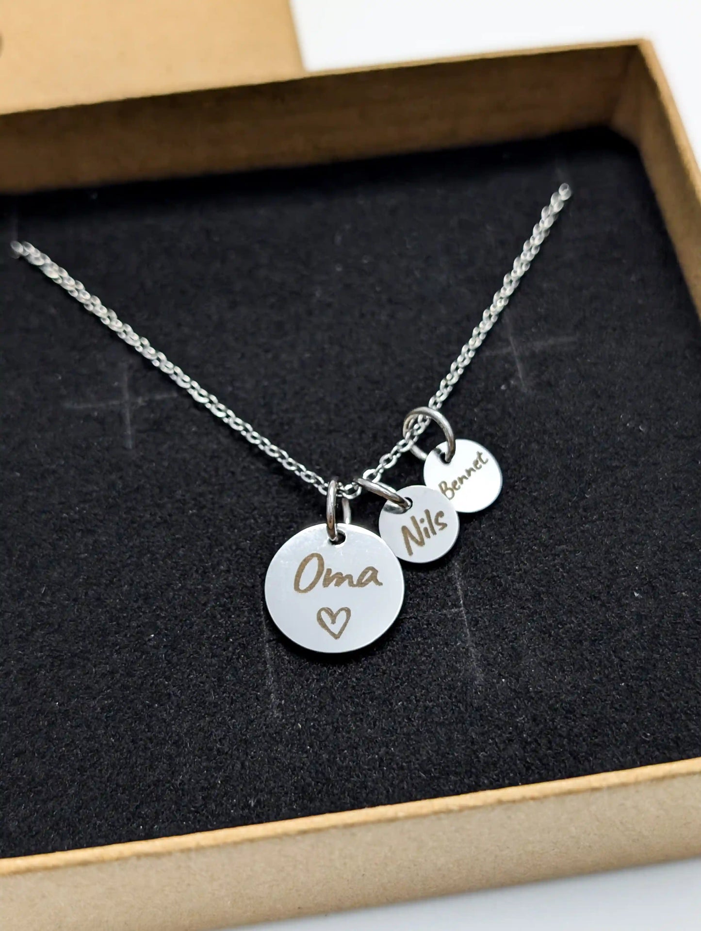 Personalisierte Oma Kette aus silbernem Edelstahl mit gravierten Namensanhängern „Oma“, „Nils“ und „Bennet“, präsentiert in schwarzem Schmuckinlay – individuelles Geschenk für Großmütter.
