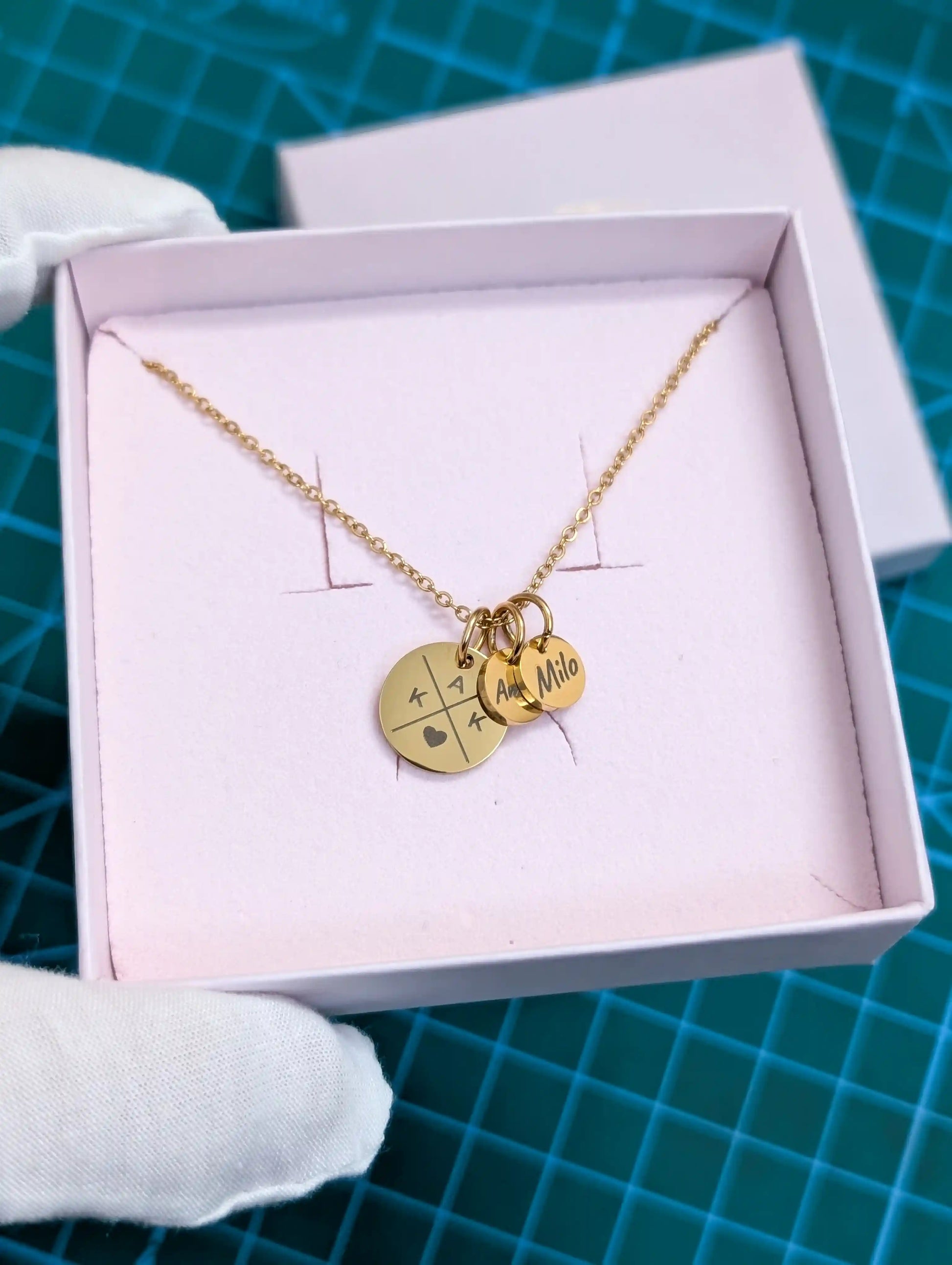 Goldene personalisierte Namenskette mit gravierten runden Anhängern, liebevoll in einer rosa Schmuckbox präsentiert – individuelles Geschenk mit Initialen und Namen.