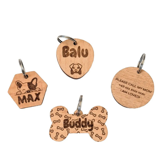 Vier personalisierte Hundemarken aus Holz. Vorne Knochenform mit Aufschrift "Buddy", dahinter ein sechseckiger Anhänger mit einem Hund und "Max", daneben ein runder Anhänger mit "Please call my mom", einer Telefonnummer und "I am loved" und ganz hinten ein ovaler Anhänger mit "Balu" und einem Hundemotiv