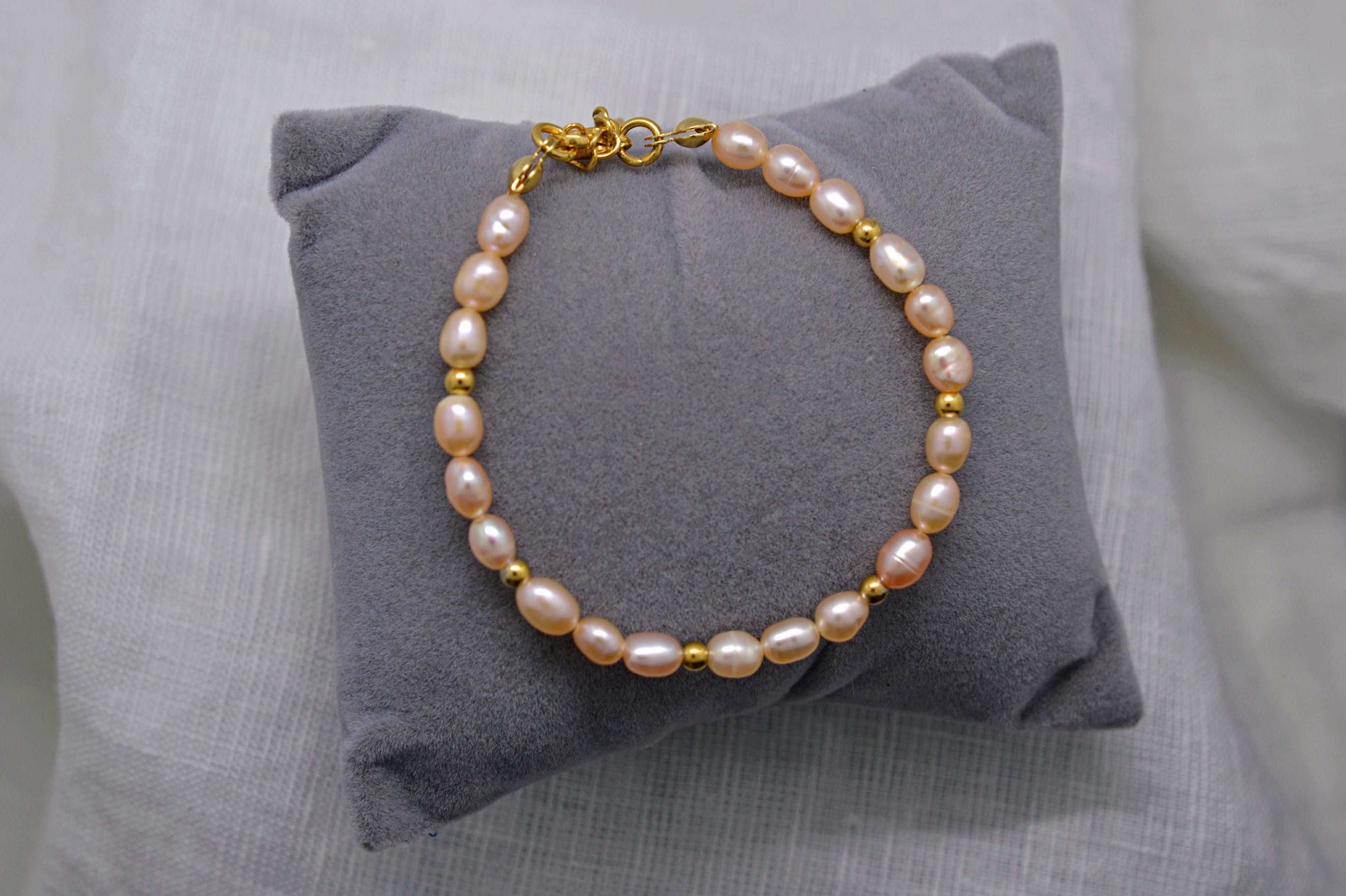 Rosafarbenes Süßwasserperlen Armband mit goldenen Perlen auf einem Schmuckkissen