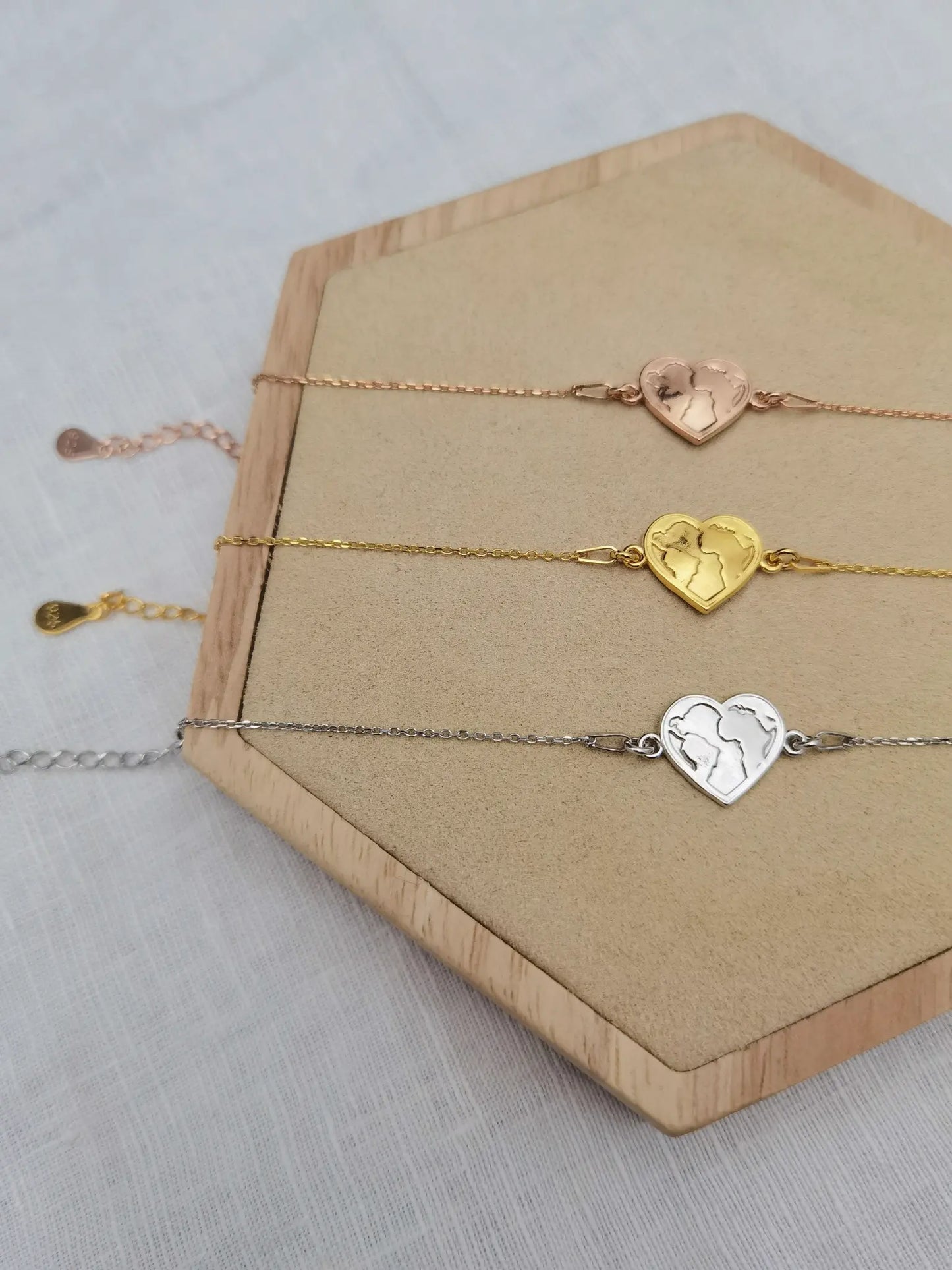 Herz Weltkarte Armband in silber, gold und roségold auf einem Holz Sechseck