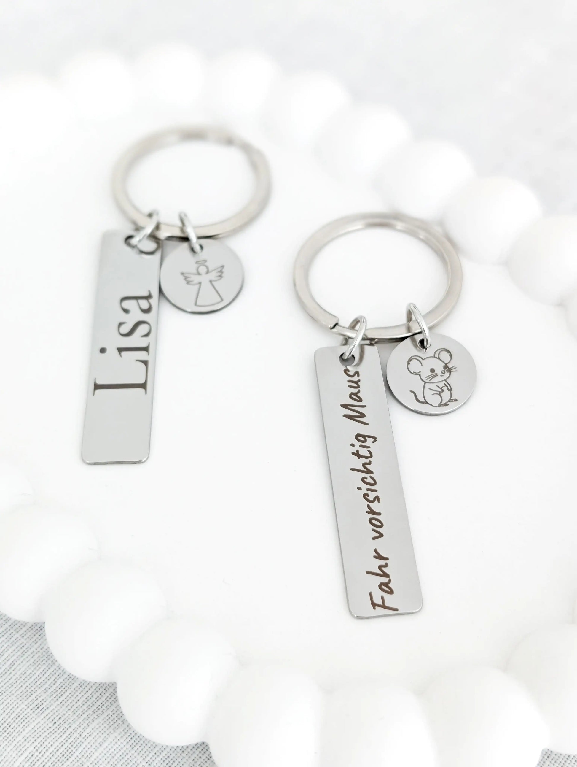 Zwei personalisierte Schlüsselanhänger aus silbernem Edelstahl mit rechteckigem Anhänger und rundem Symbol-Anhänger, graviert mit ‚Lisa‘ und einem Engel sowie ‚Fahr vorsichtig Maus‘ und einer kleinen Maus – individuelle Geschenkidee für Kinder, Mama oder Fahranfänger.