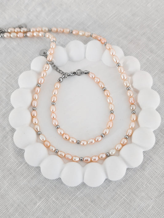Schmuckset aus rosa Süßwasserperlen mit silbernen Akzenten. Süßwasserperlen Kette und Armband auf einem weißen Schmuckuntersetzer fotografiert
